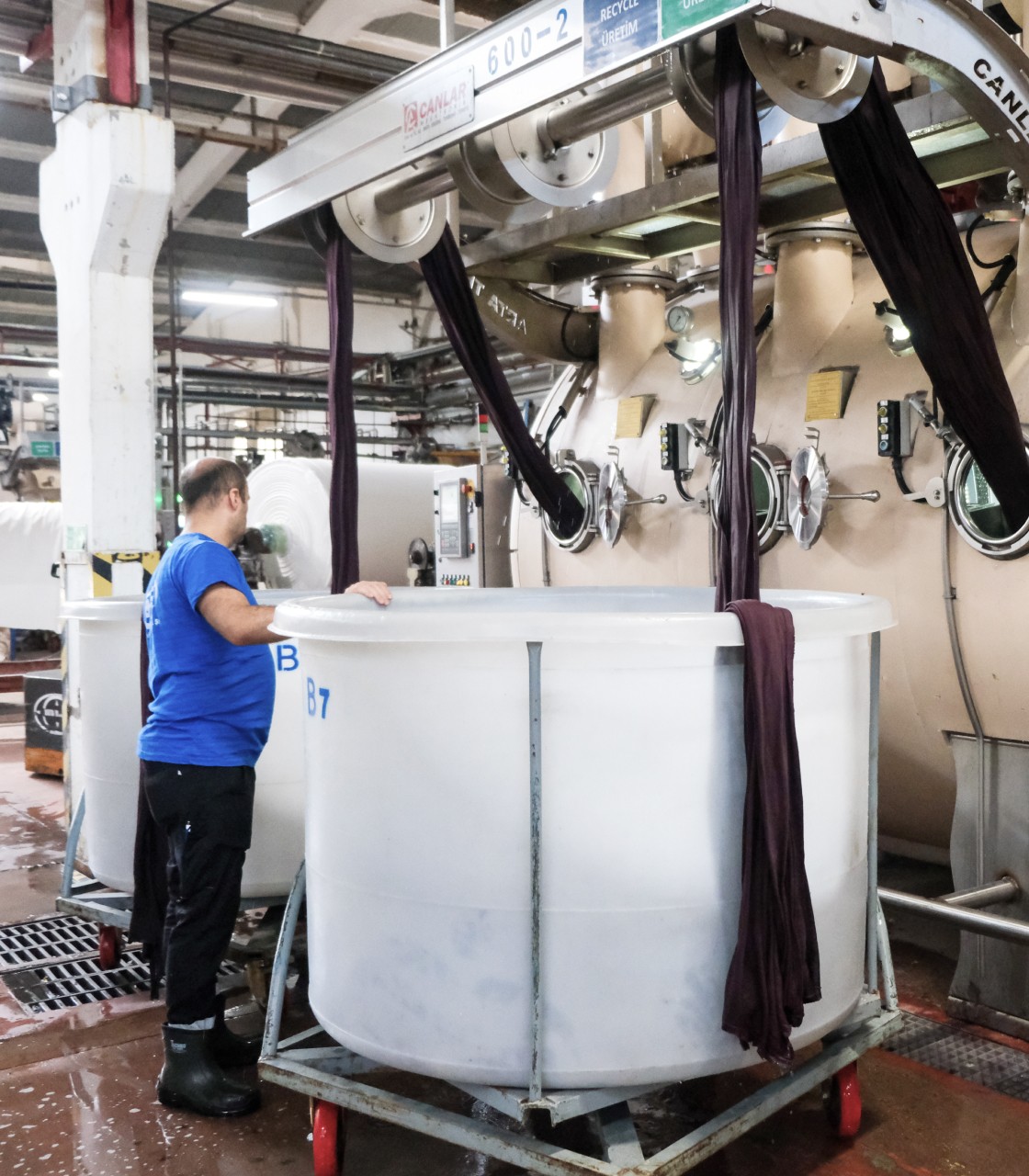Textile dyeing machine and factory worker handling fabric in garment production facility