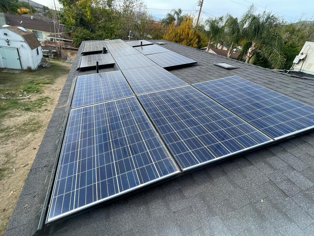A modern house with large windows and a flat roof, surrounded by greenery against a clear blue sky.