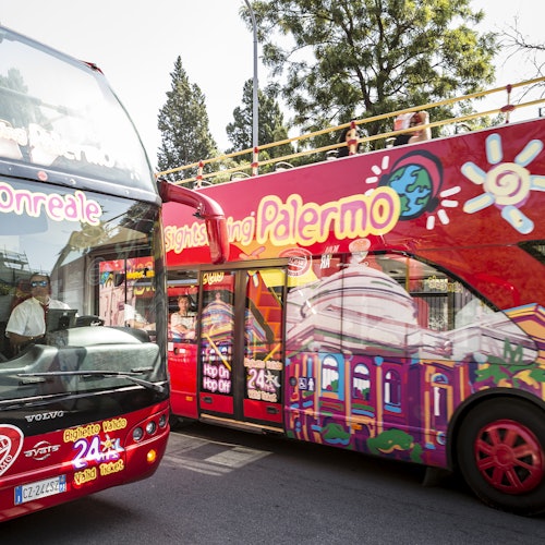 パレルモで見られる、「観光－パレルモ」と明るくデザインされた文字が書かれた2台の赤い二階建て観光バス。周囲には木々と人々が見えます。