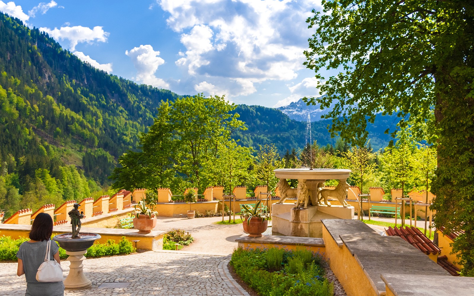 Visitor exploring Hohenschwangau Castle garden with mountain view.