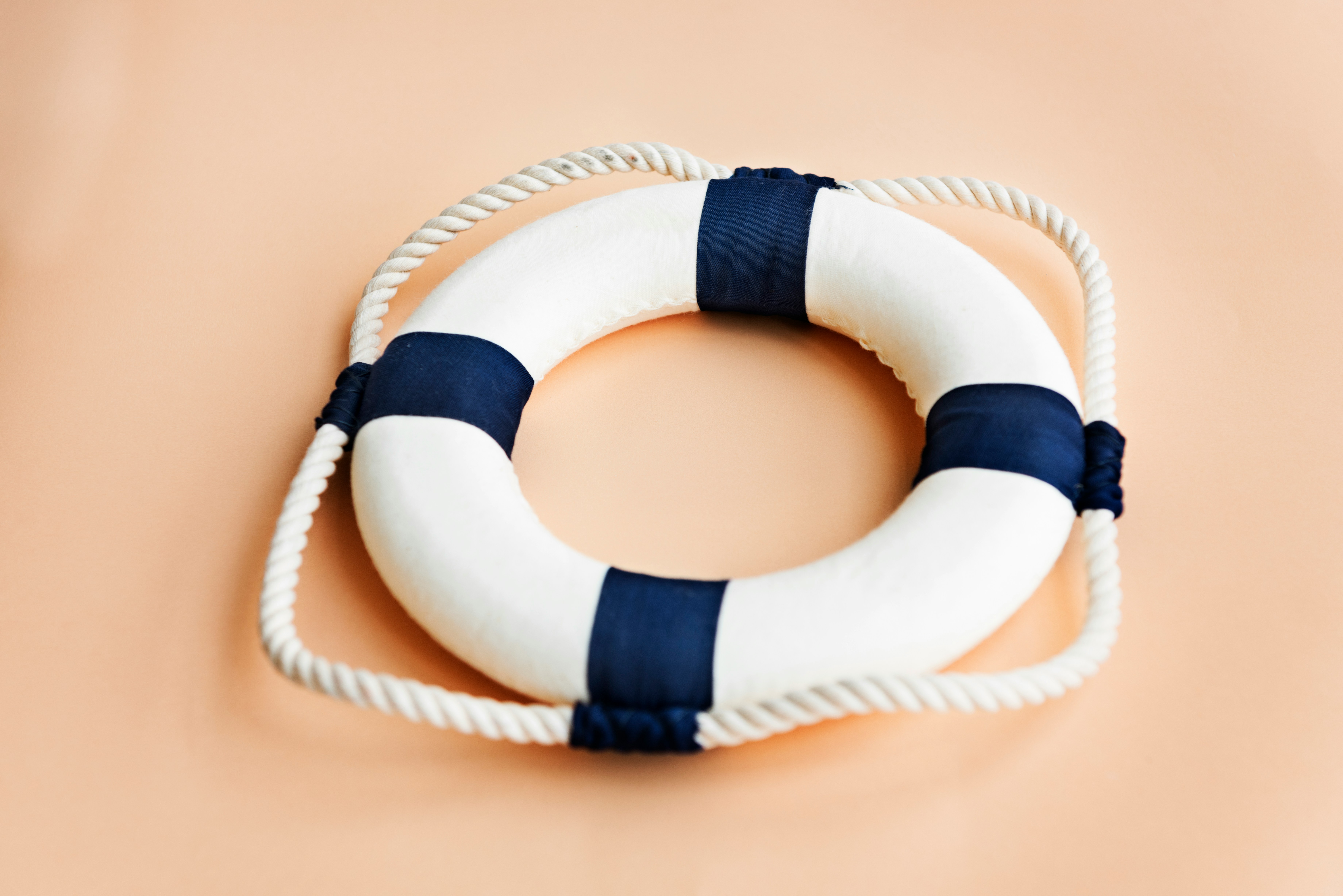 White and dark blue lifebuoy with a wrapped safety rope against a neutral beige background.