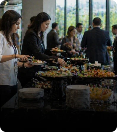 Buffet para almoço e coquetel corporativo com convidados se servindo em evento empresarial sofisticado e clima de networking profissional.