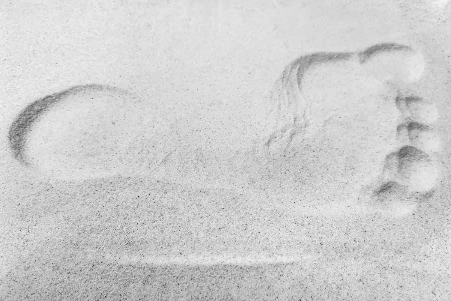 A close-up of a single bare footprint pressed into pale sand.