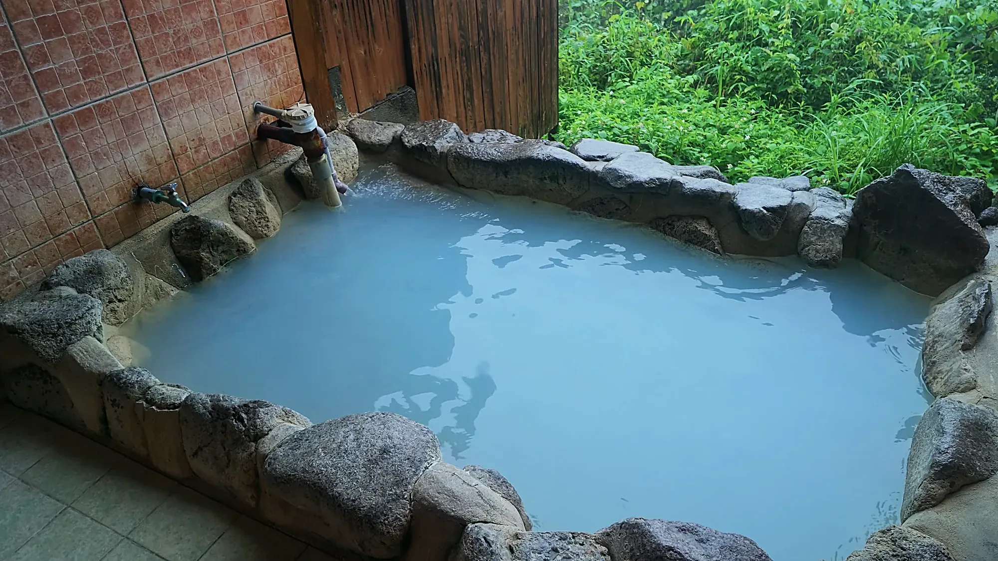 A milky blue pool with a brick and stone rim among greenery