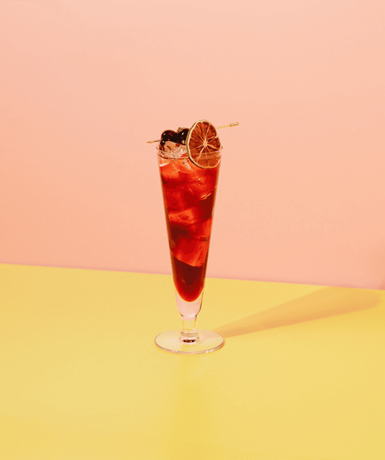 A deep red mocktail in a glass, garnished with dired lime and cherries