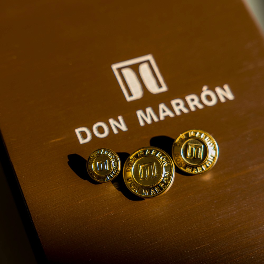 Close-up of a hand holding a DM-engraved button against a tailored jacket, capturing the fine craftsmanship, precision, and artistry that define luxury tailoring.
