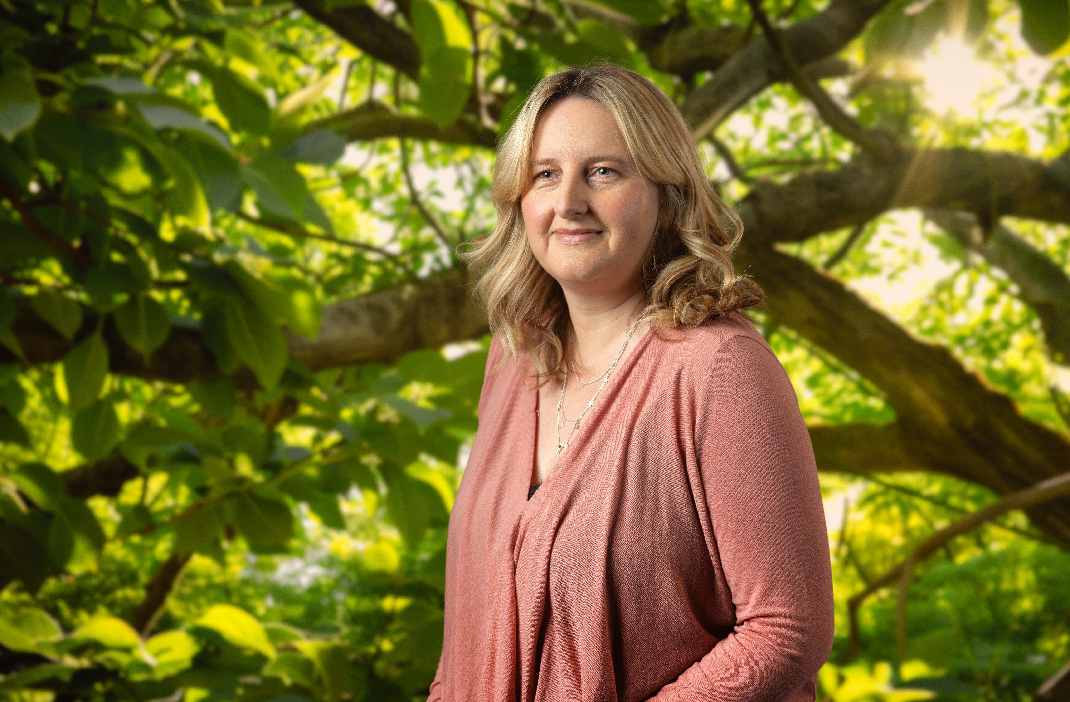 Smiling female therapist with short gray hair, wearing a brown top and a purple shawl, surrounded by a cozy background.