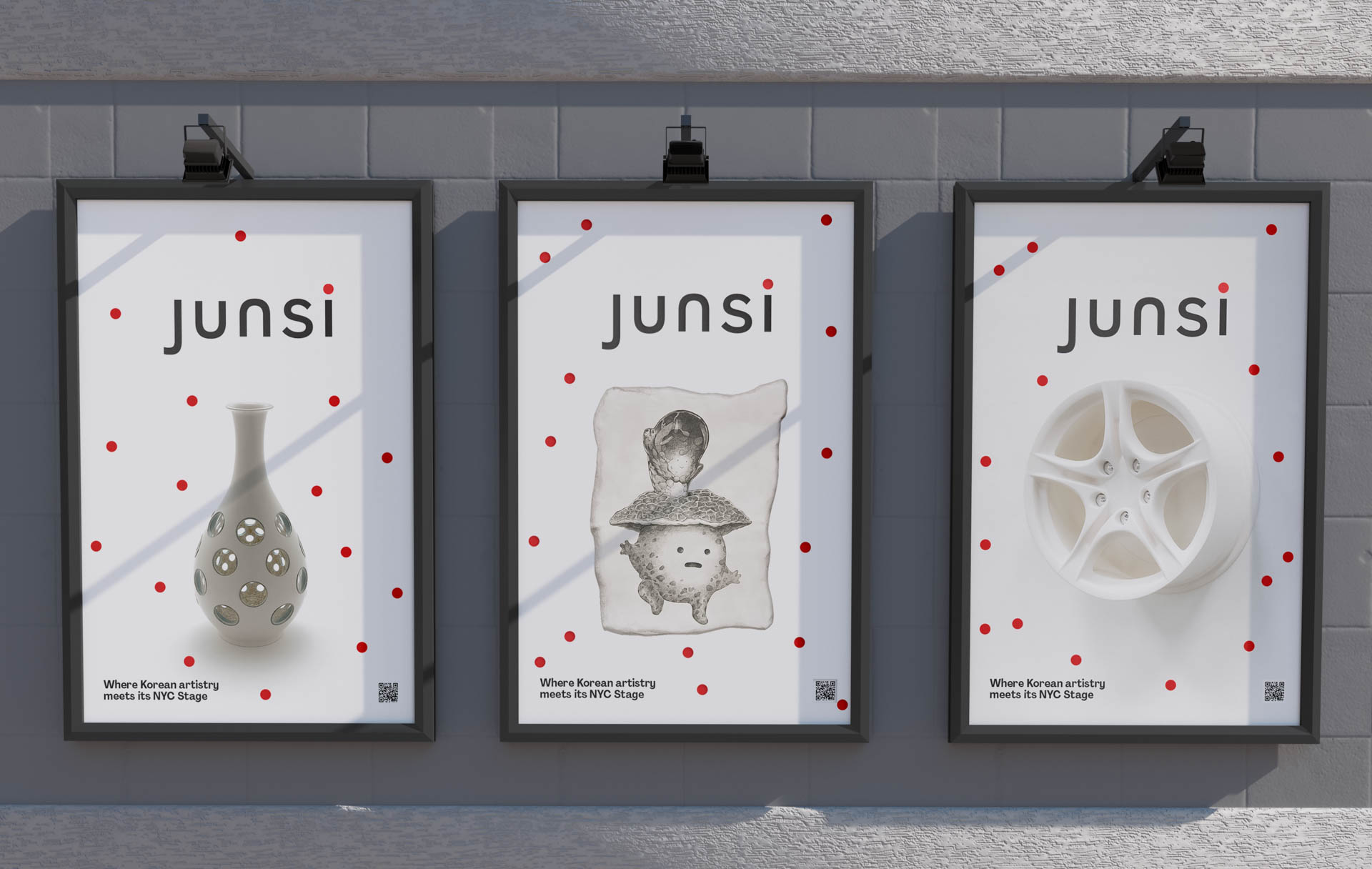 Three framed posters are mounted on a gray brick wall. Each poster features the word "JUNSI" in black letters on a white background, with a red dot pattern surrounding it. The left poster shows a gray vase with small holes. The center poster displays a black and white illustration of a stylized figure on a pillow. The right poster shows a white wheel with red dots. Below each poster, a small text block reads “Where Korean artistry meets its NYC Stage.” A QR code appears at the bottom right of each poster.
