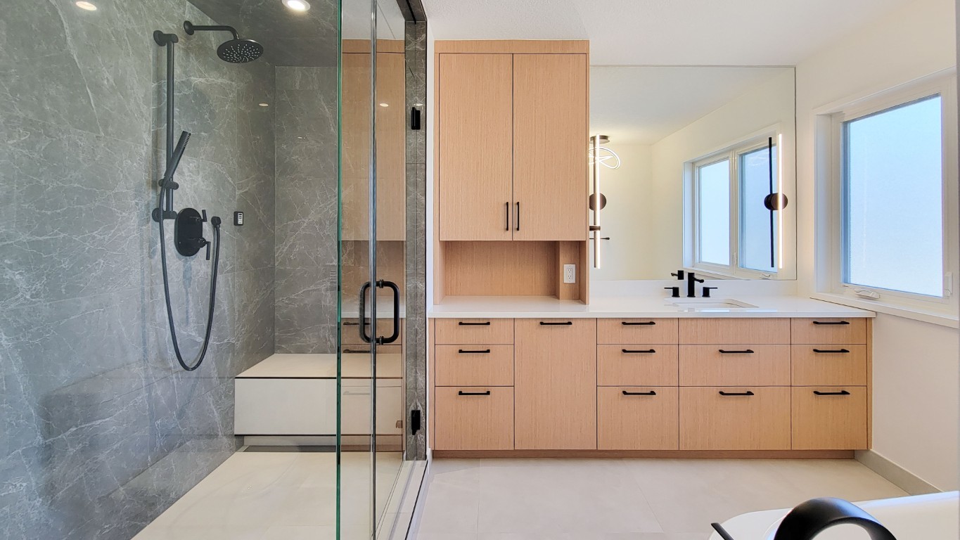 Image of Modern primary ensuite bathroom with marble shower, wooden cabinets, and large mirror by KHD Homes design-build.