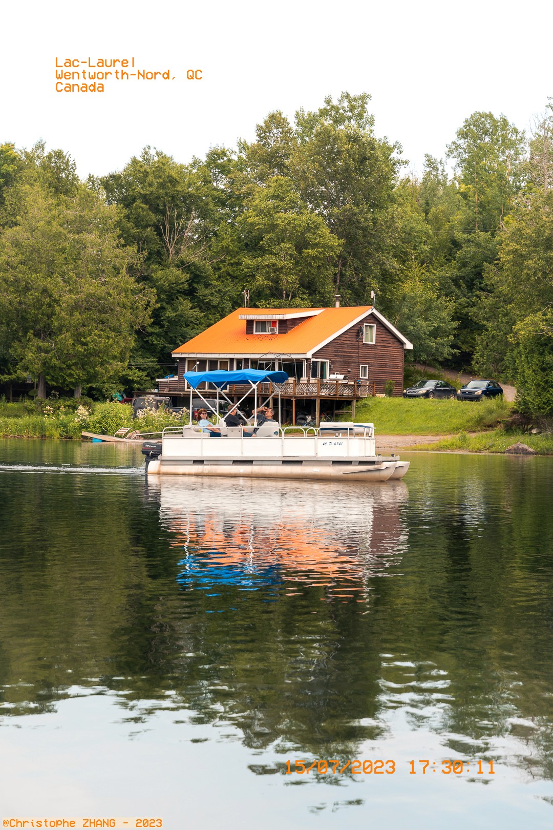 Bateau de plaisance passant devant un chalet en bois avec un toit orange vif sur le lac Laurel.
