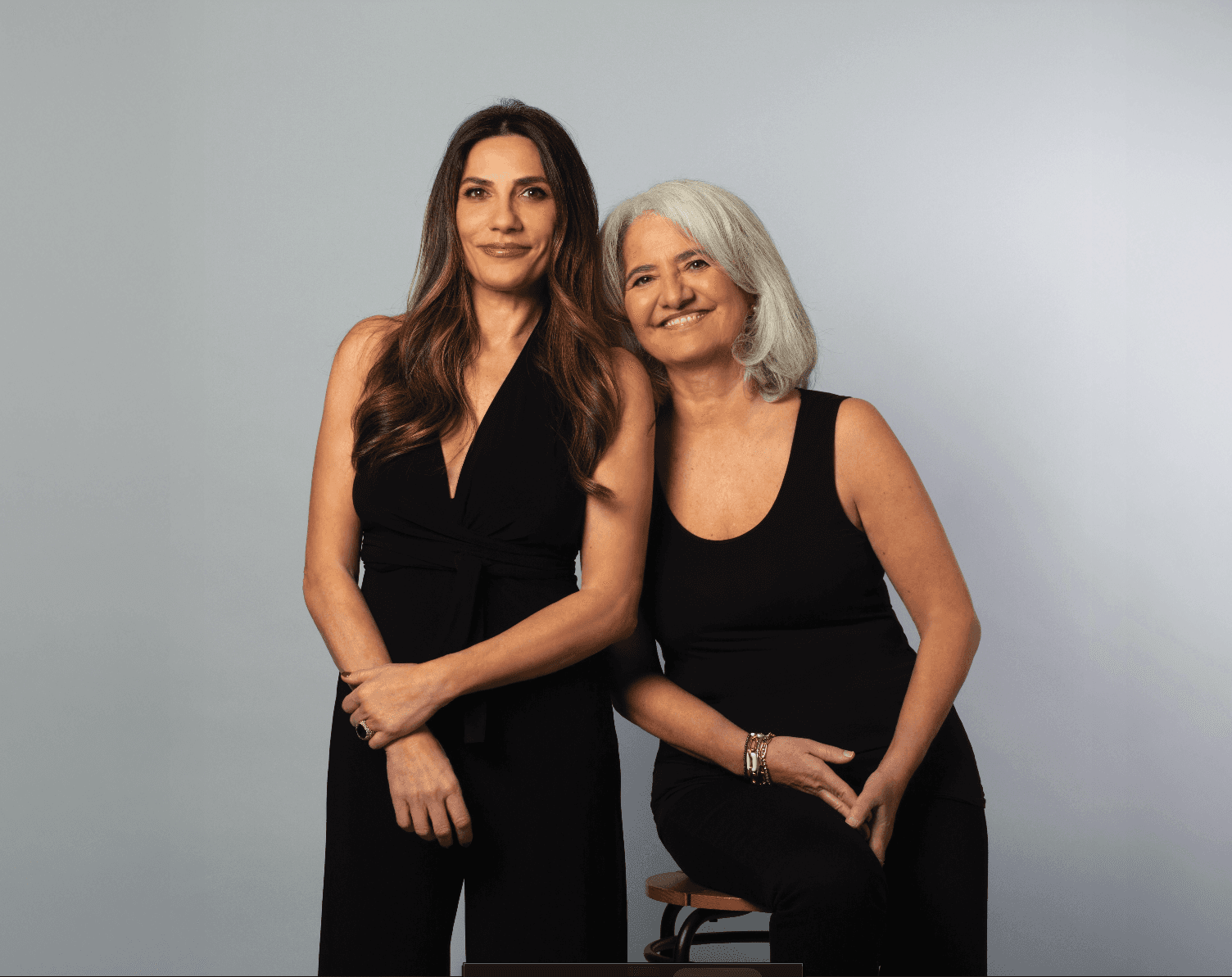 A young person with curly hair smiles at the camera while sitting in front of a laptop against a dark background.