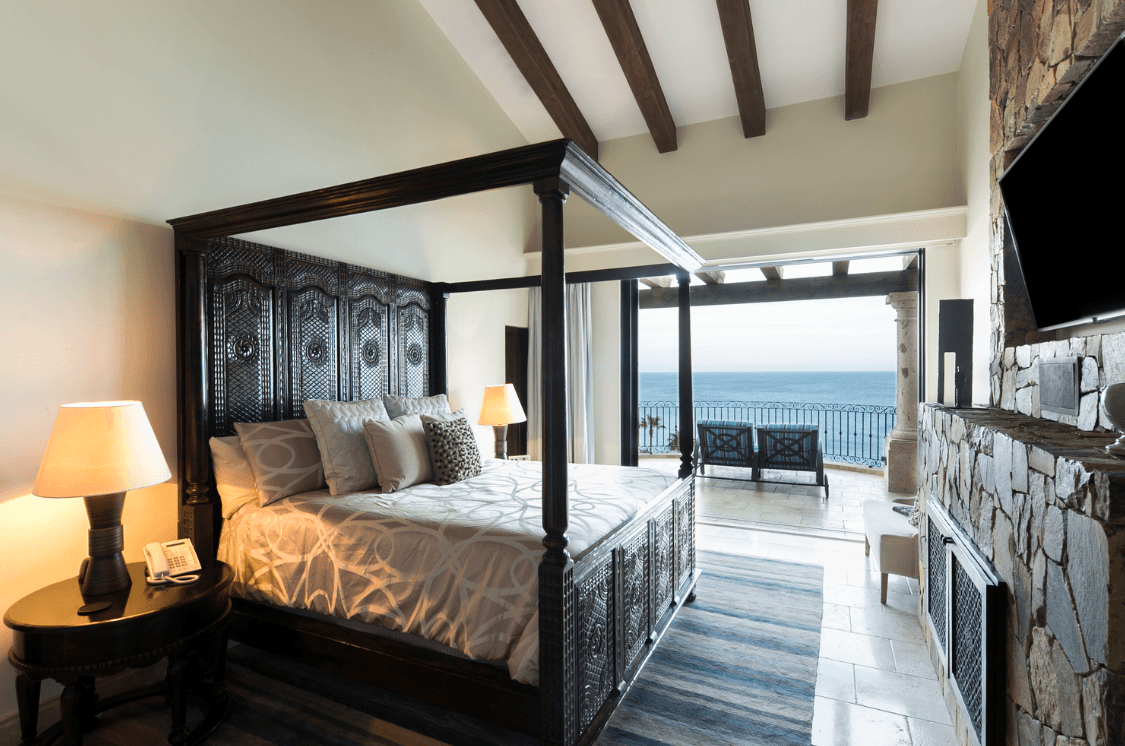 Bedroom with four-poster bed and ocean-facing windows.