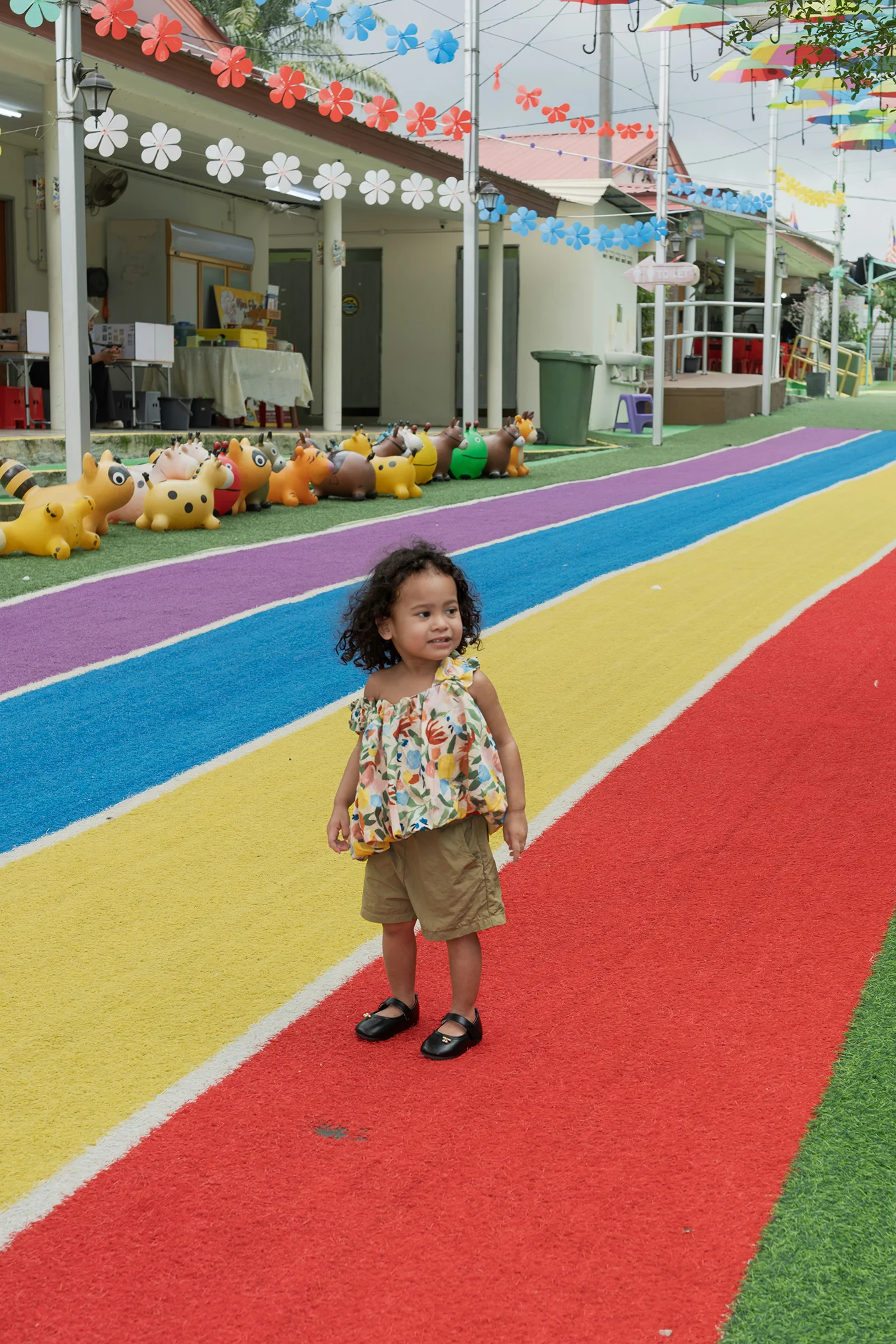 Preschool teacher guiding a young child outdoors in a green and open play area