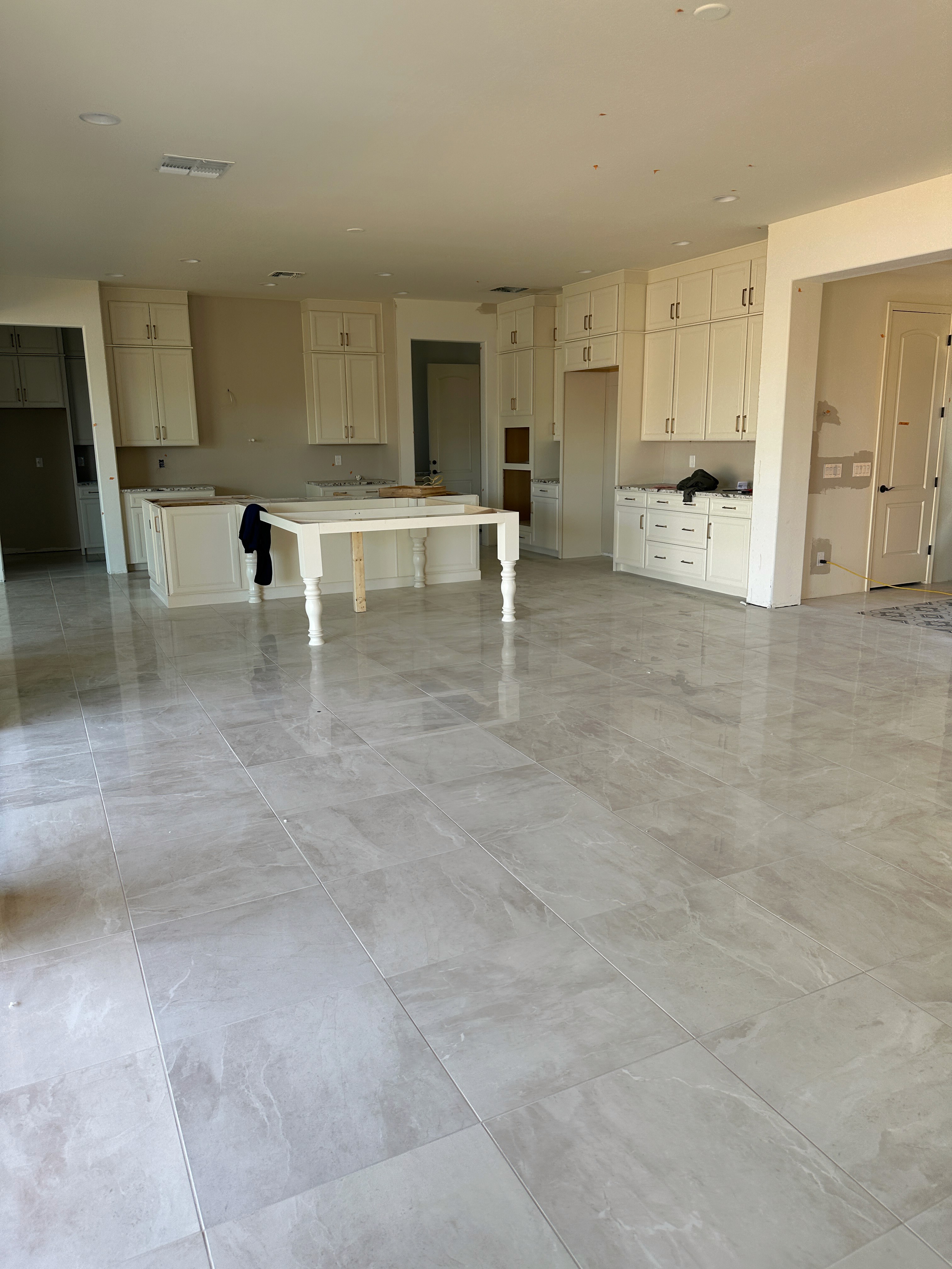 Modern open-plan living area with glossy marble tiles, white cabinets, and a central table in a new home under construction.