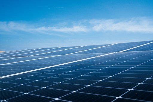 Solar panels reflecting sunlight under a clear blue sky with scattered clouds in the background.