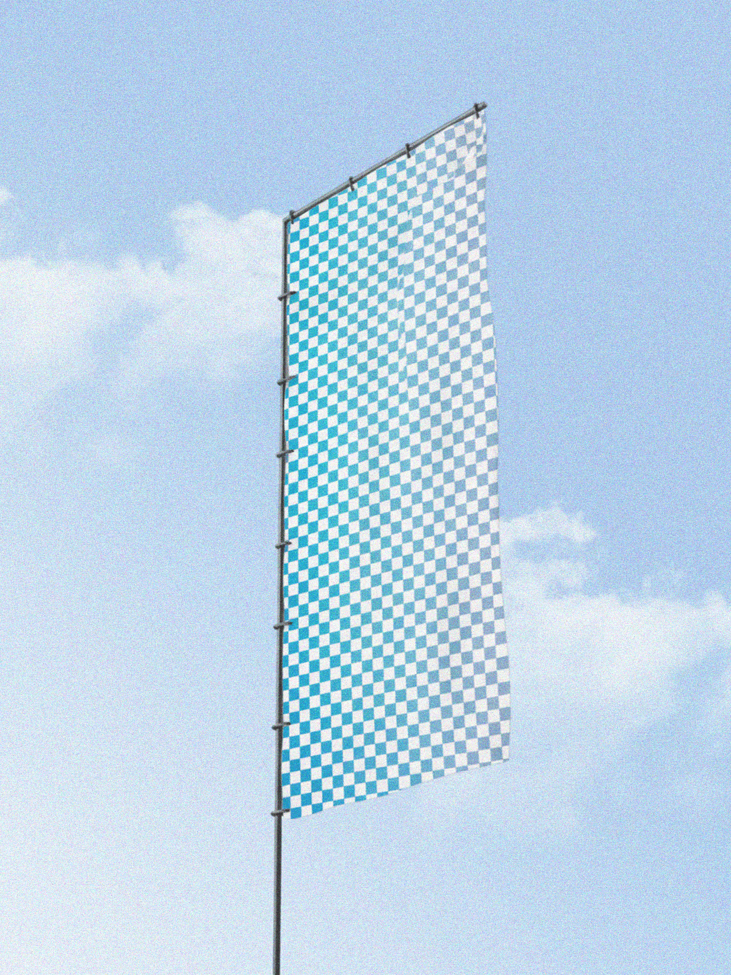 A tall outdoor flag with a blue-and-white checkered pattern, waving gently against a soft sky.