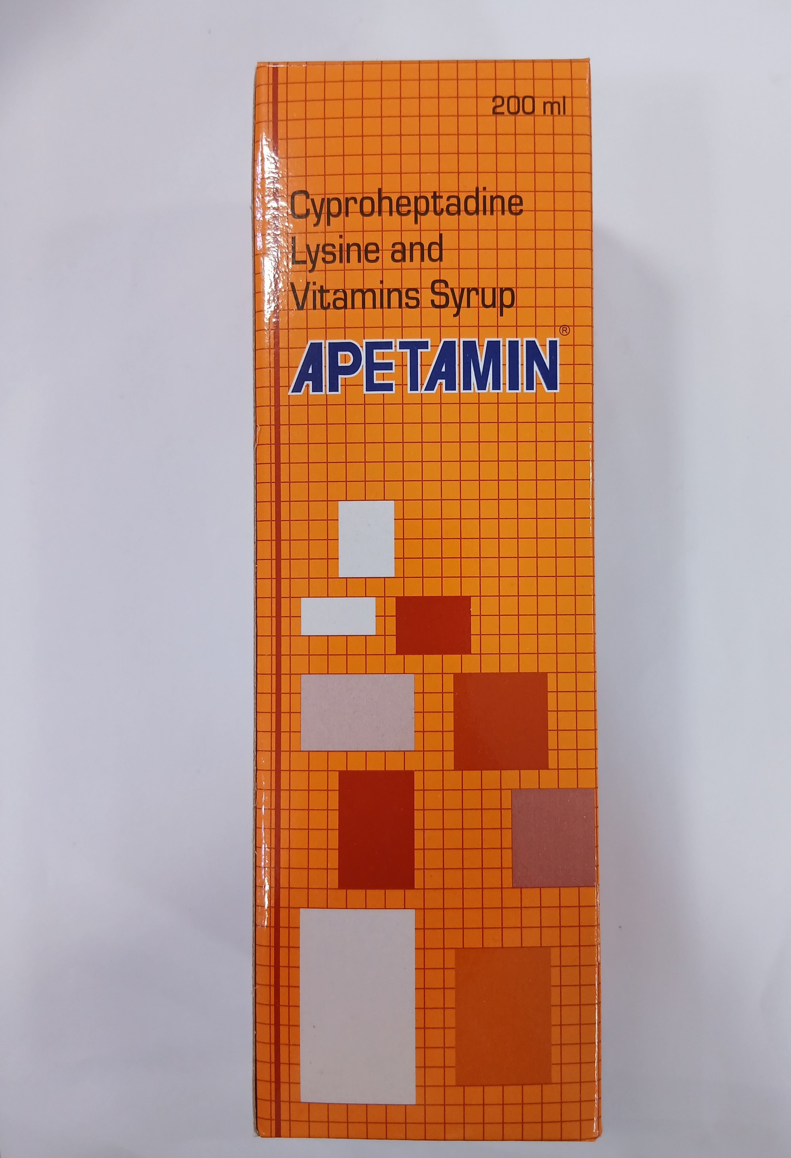 The image shows an orange cardboard box with a grid pattern background and printed white and red square graphics, containing a 200 milliliter bottle of cyproheptadine lysine and vitamins syrup.