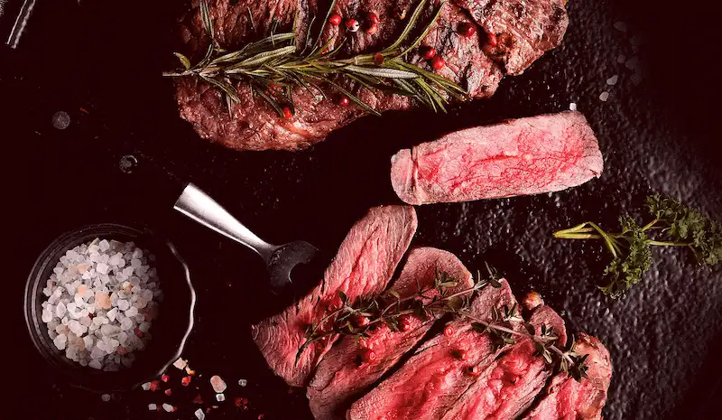 Modern indoor space with large glass doors, lush greenery, and a cozy seating area visible beyond.