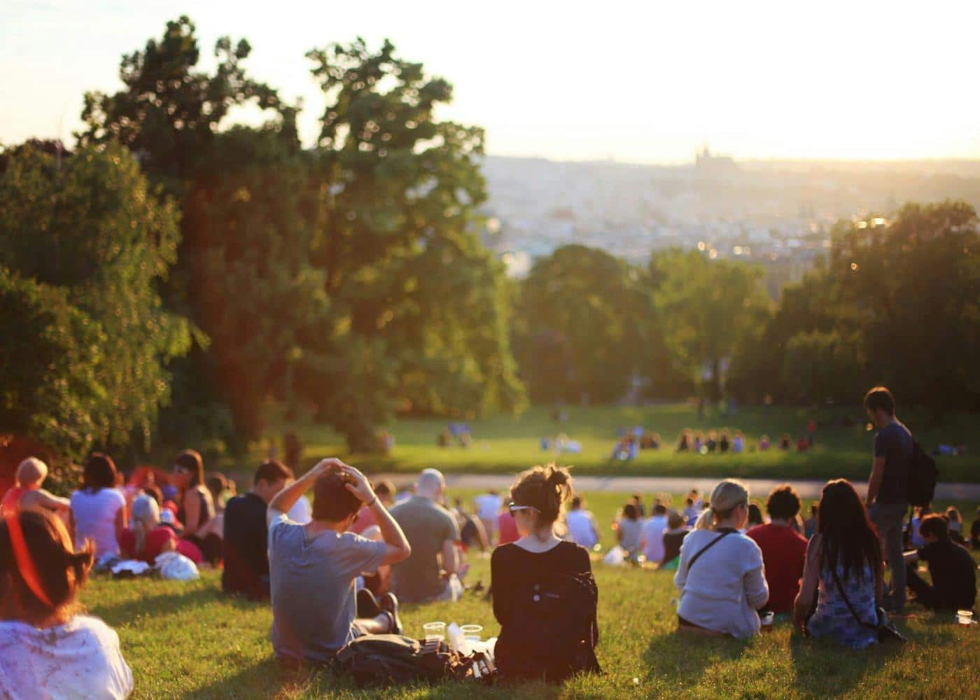 people sitting on the grass in a park and watching the sunset