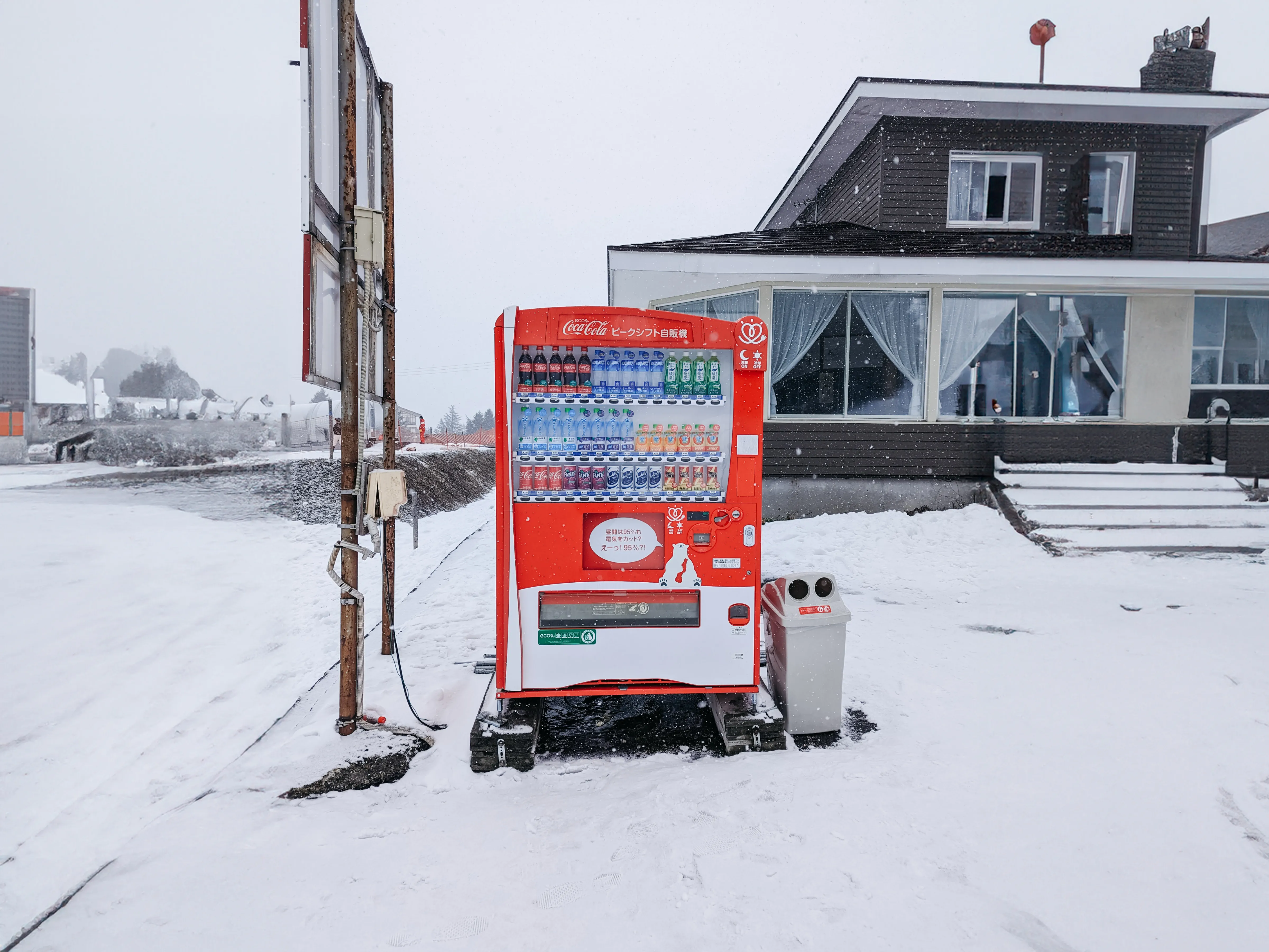 A red Coca-Cola vending machine outside a Japanese ski lodge in the snow