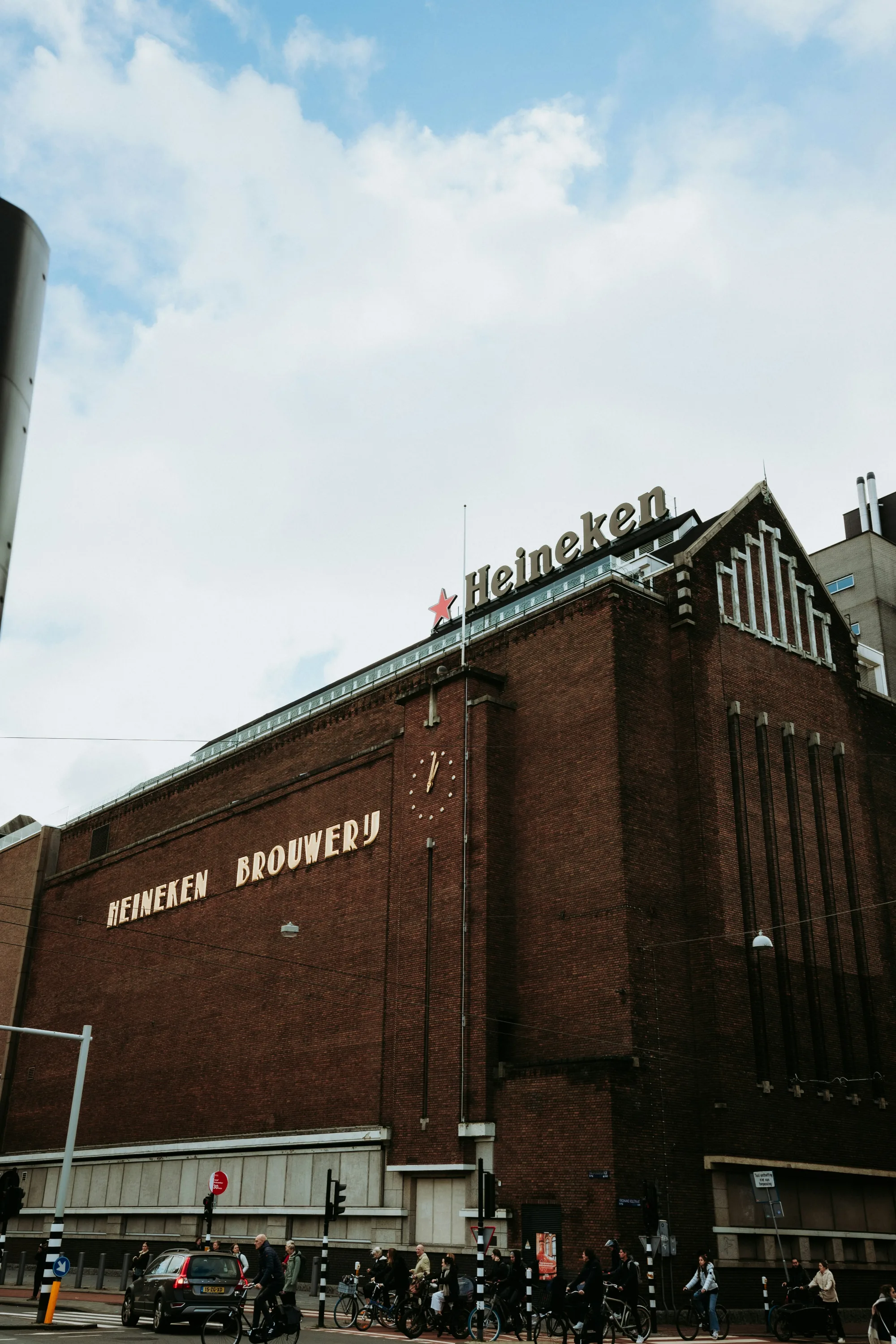 The historic Heineken Brewery building in Amsterdam, with the iconic red star and branding visible under a cloudy sky.