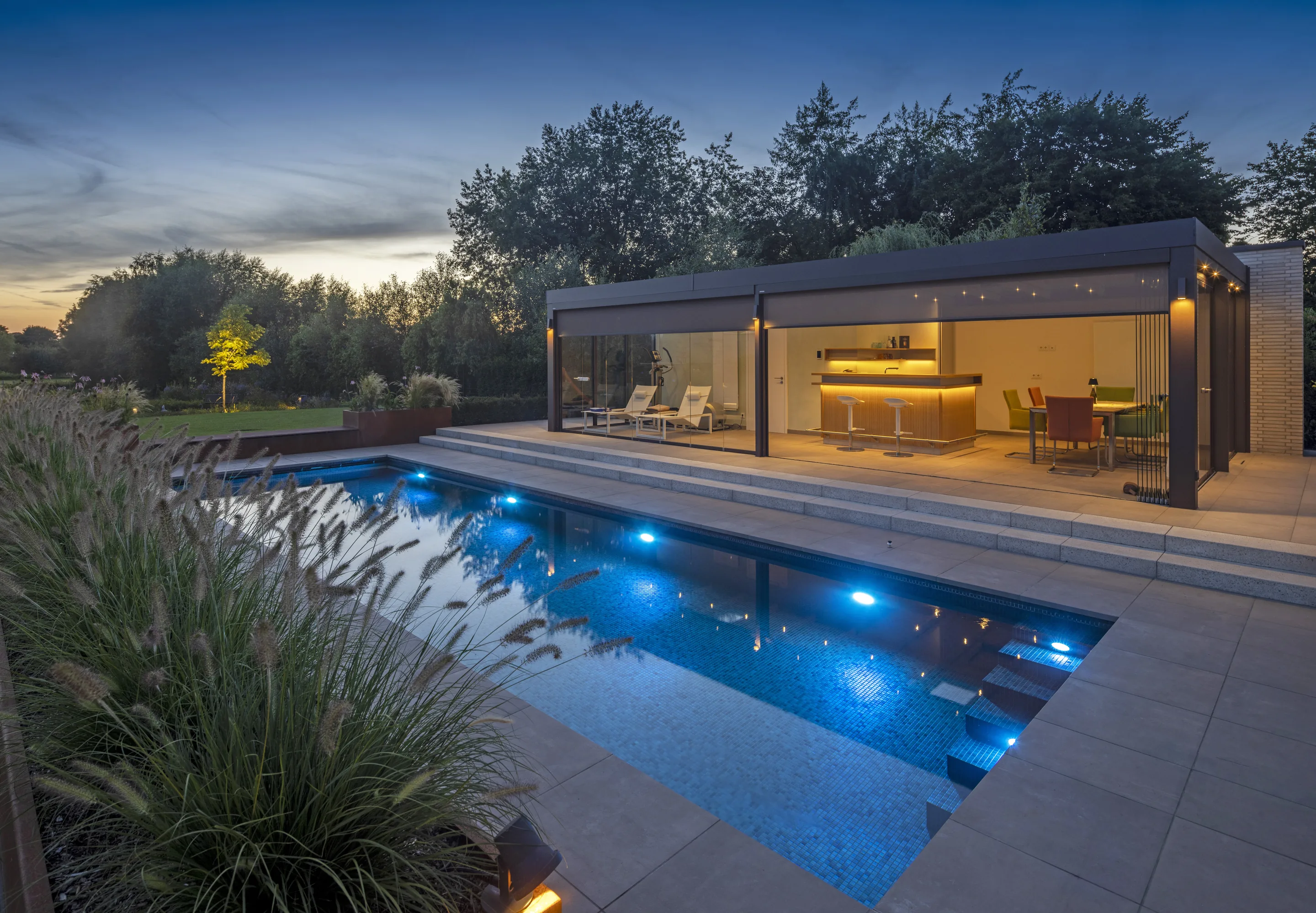 MLine swimming pool in the evening with a modern pool house, LED lighting, and string lights