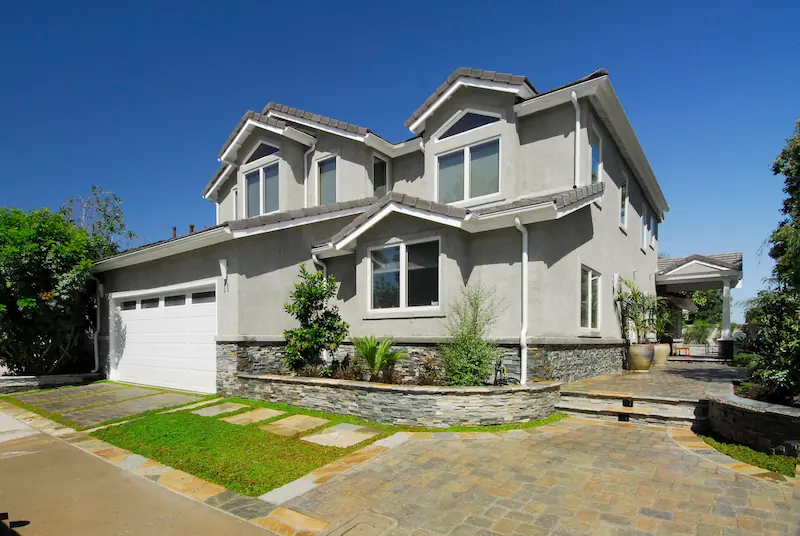 Modern two-story house with a gray facade and stone accents, clear skies above. Photo by Chris Darnall for Irvine Transitional Modern.