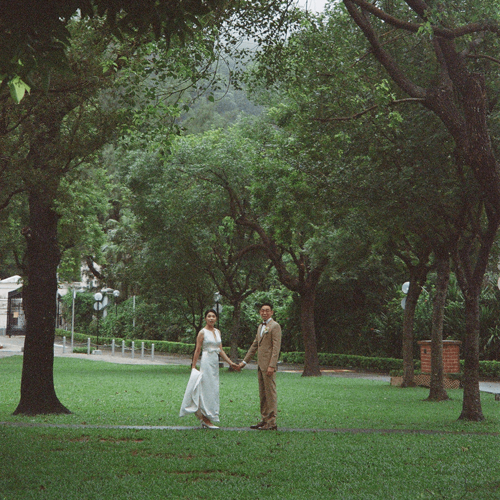 A wideshot of a pair of couples on their wedding day looking at the camera in the wooded environemnt of tall trees and green grass