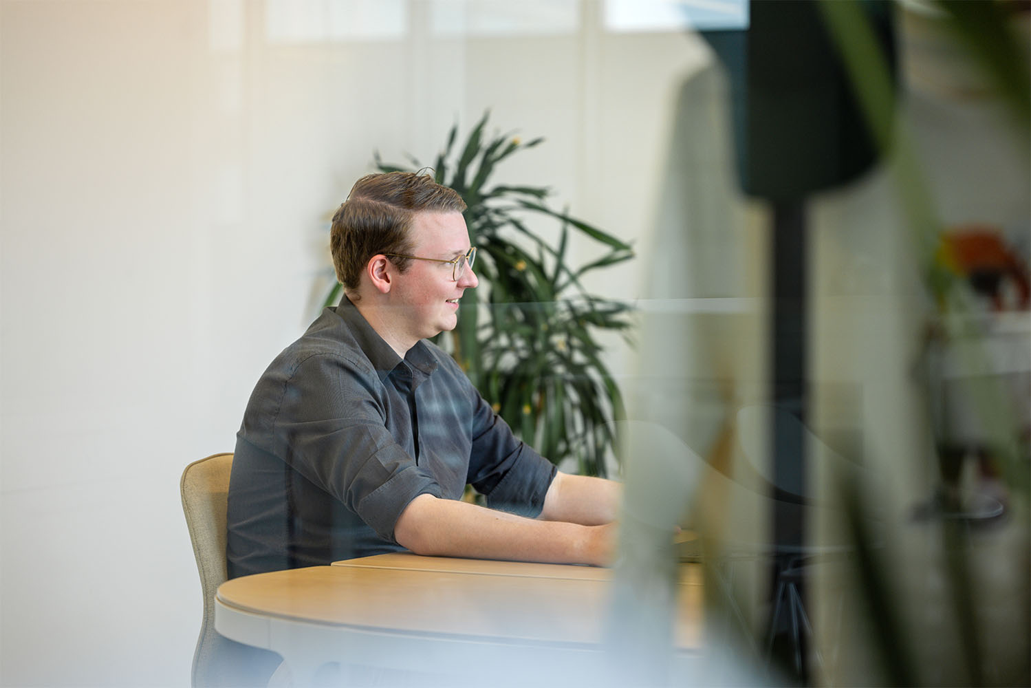 A man sits at a table with a plant in the background, engaged in a conversation.