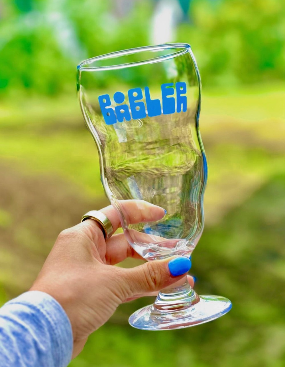 Female hand holding bubble-shaped beer glass with the logo for Båbler in blue.