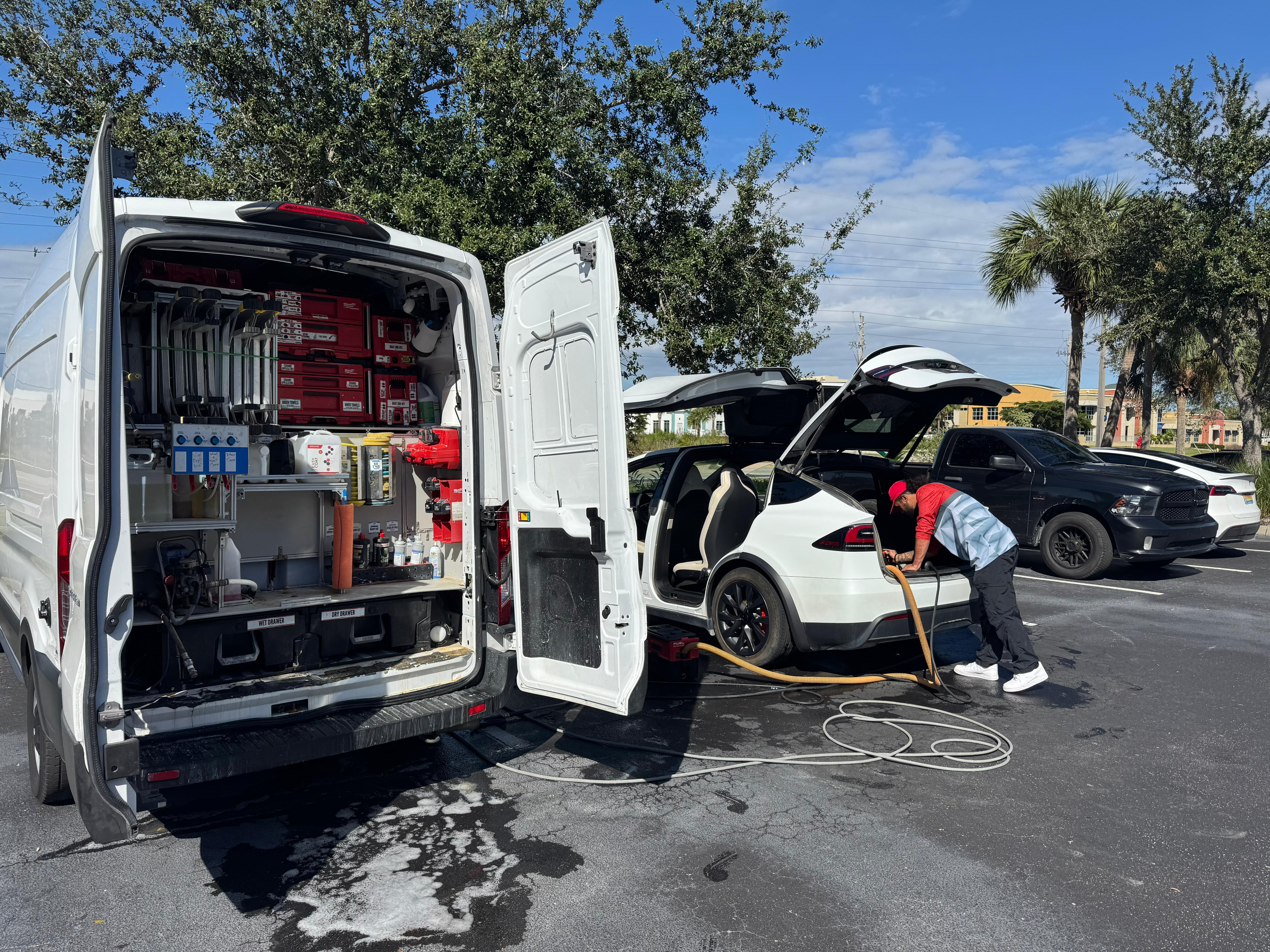 Professional auto detailer performing a foam wash on a black 2024 Tesla Model X Plaid in a Fort Myers driveway
