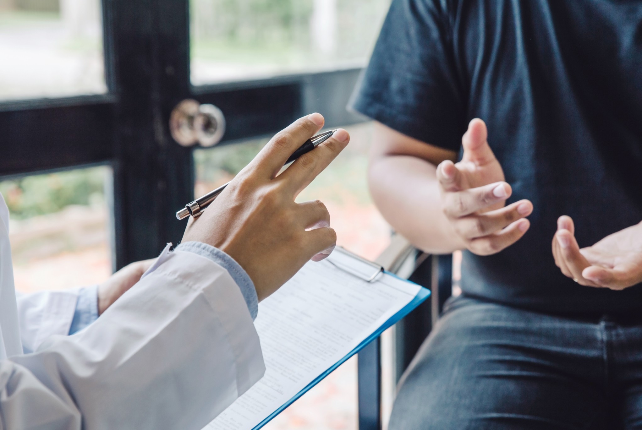 Close-up of a healthcare professional holding a pen and clipboard while discussing with a patient, representing improved patient care through revenue cycle analytics.