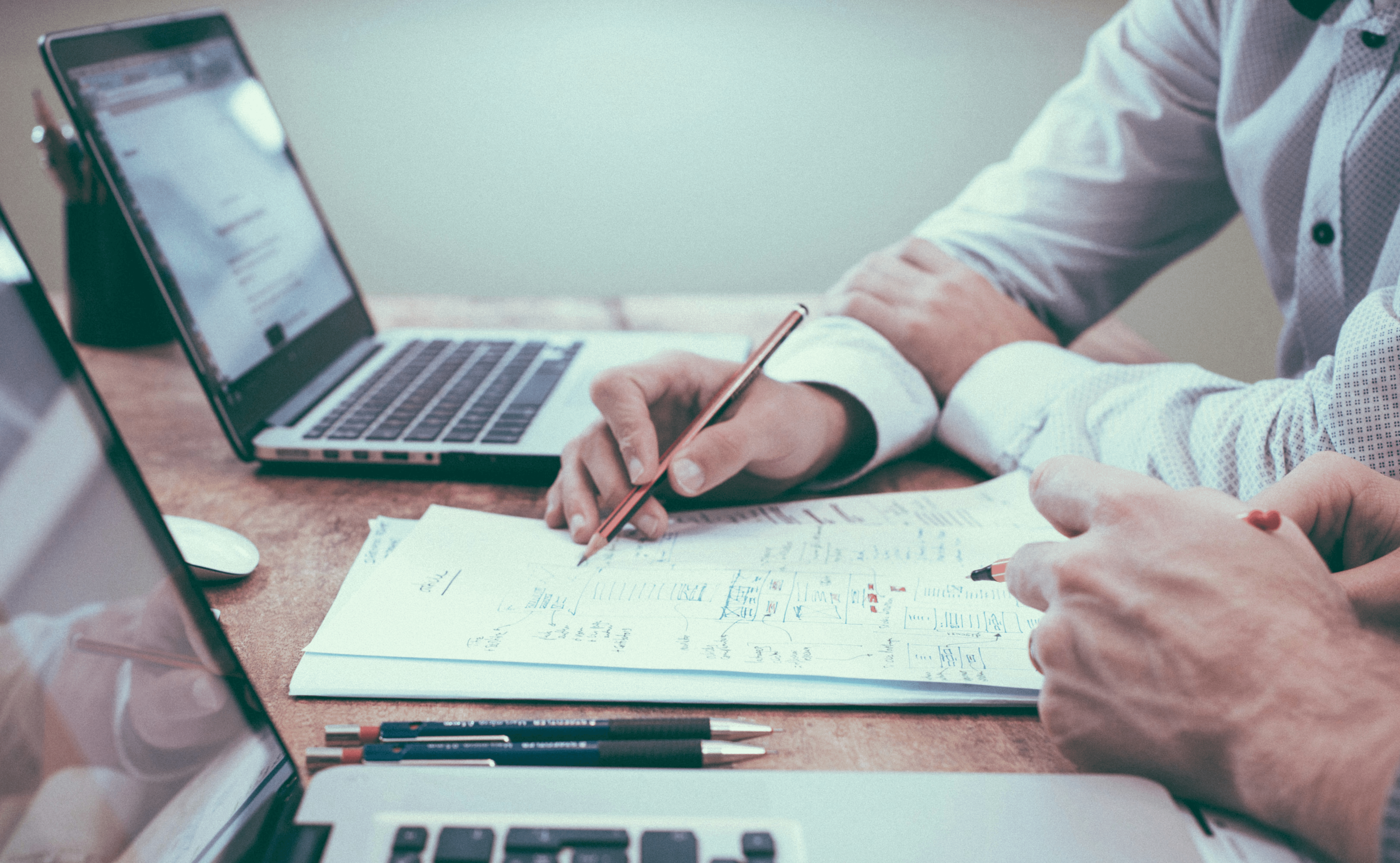 person holding pencil near laptop computer