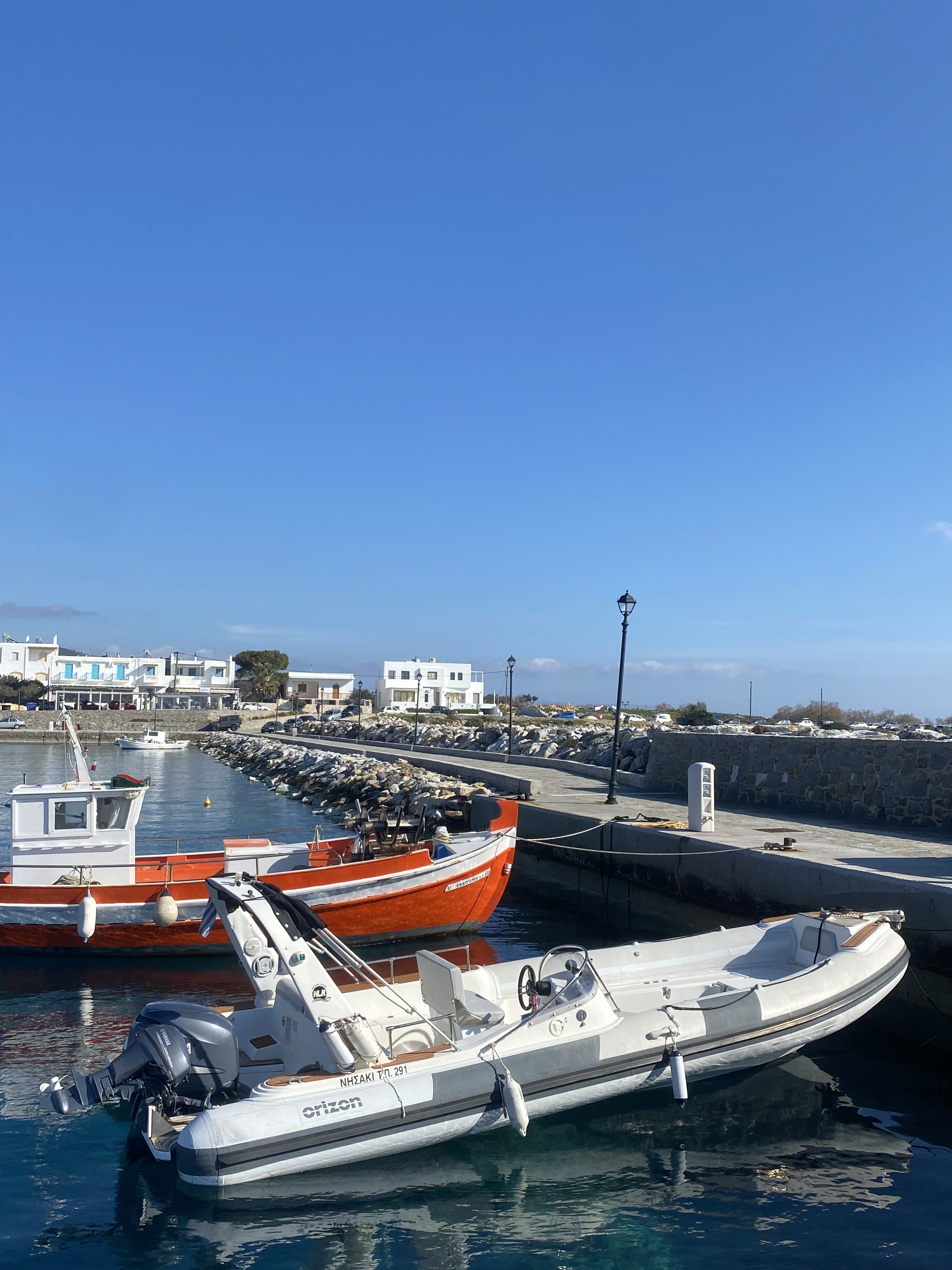 White Orizon inflatable speedboat moored in a Greek harbor with traditional fishing boats and Cycladic buildings in the background.