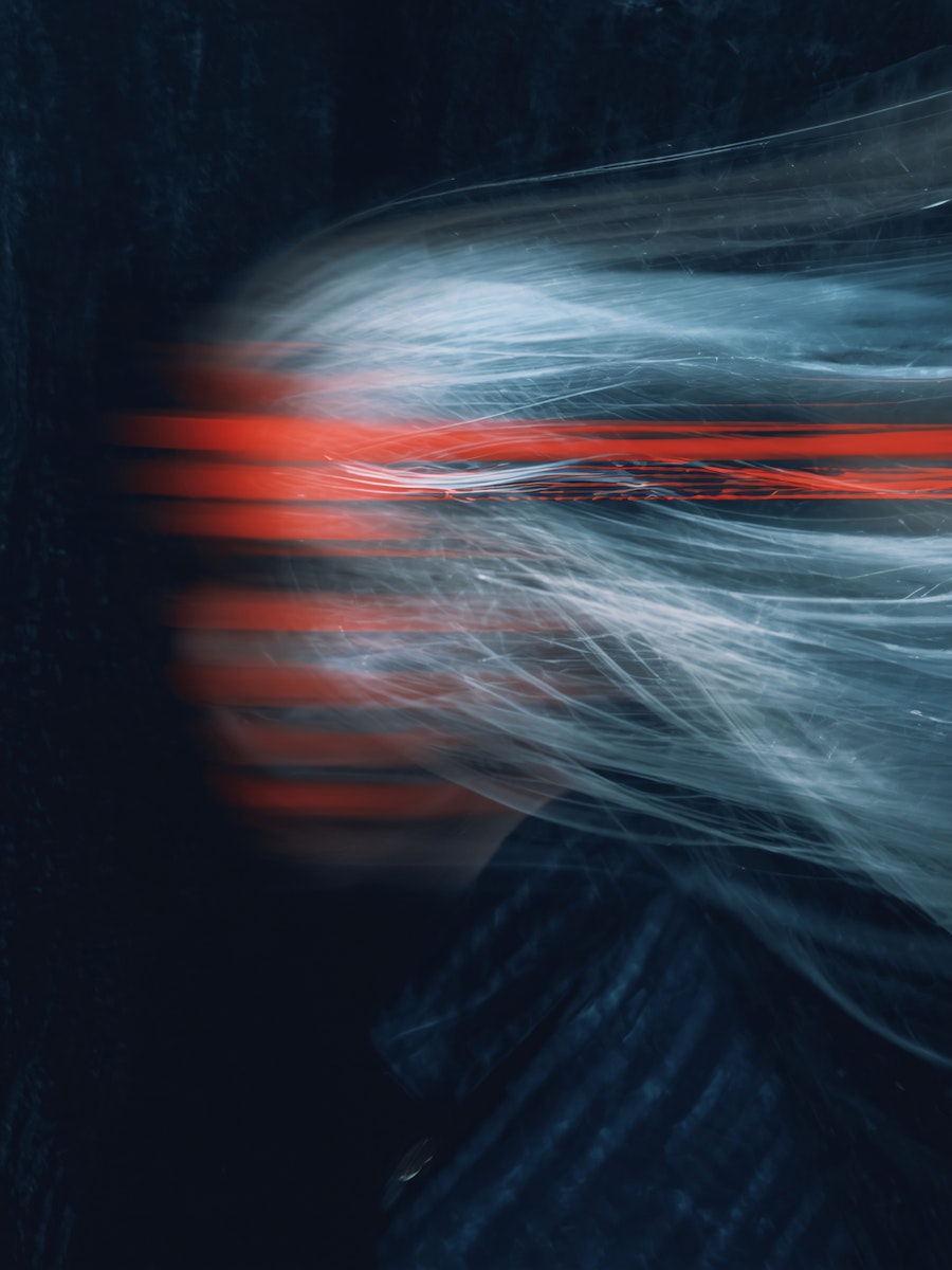 A blurred figure appears against a dark background, with streaks of light creating a dynamic, ethereal effect.
