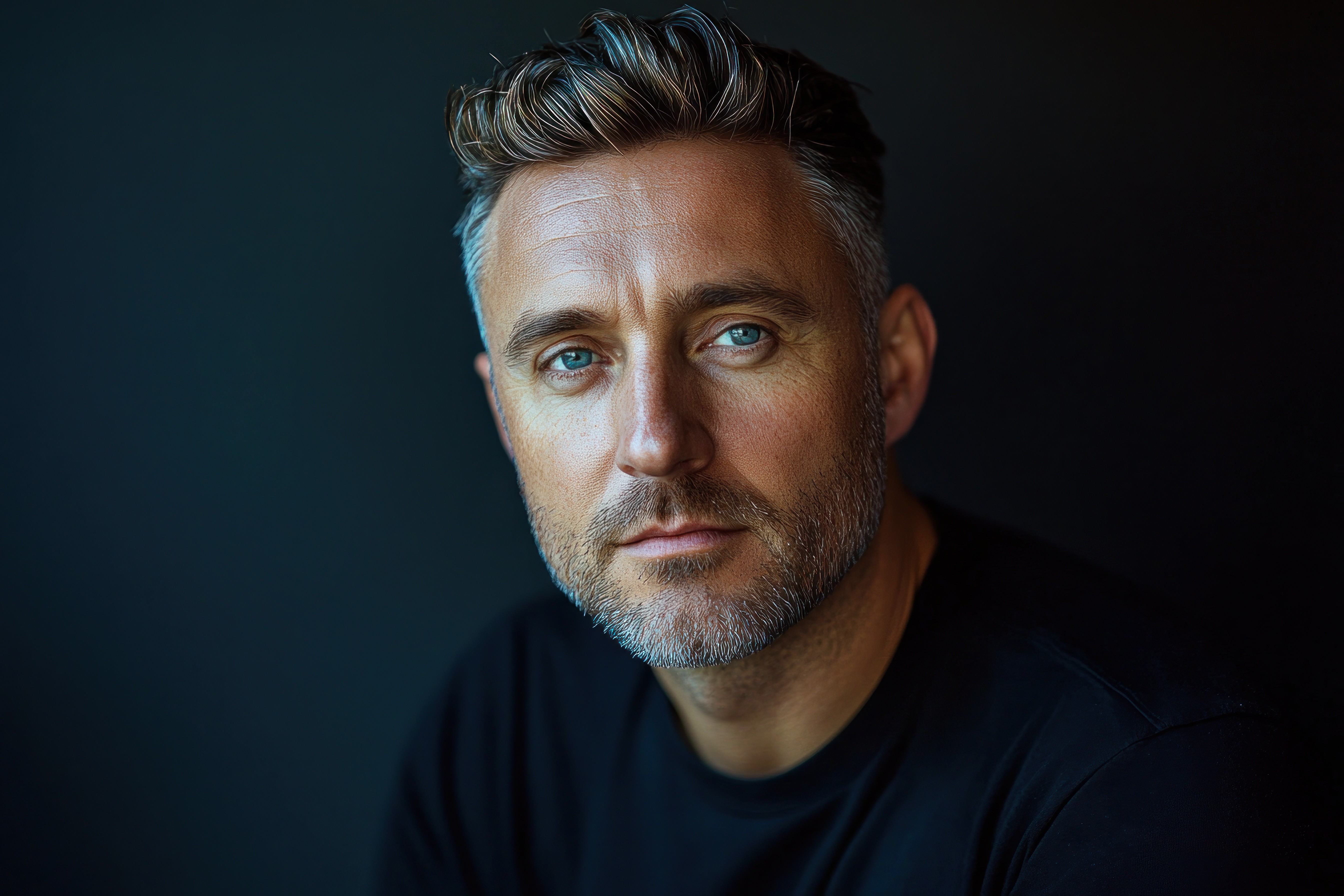 Man with blue eyes and short gray hair poses against a dark background in a simple black shirt.