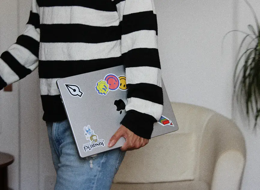 Close up of Karim holding his macbook laptop, walking towards the left.