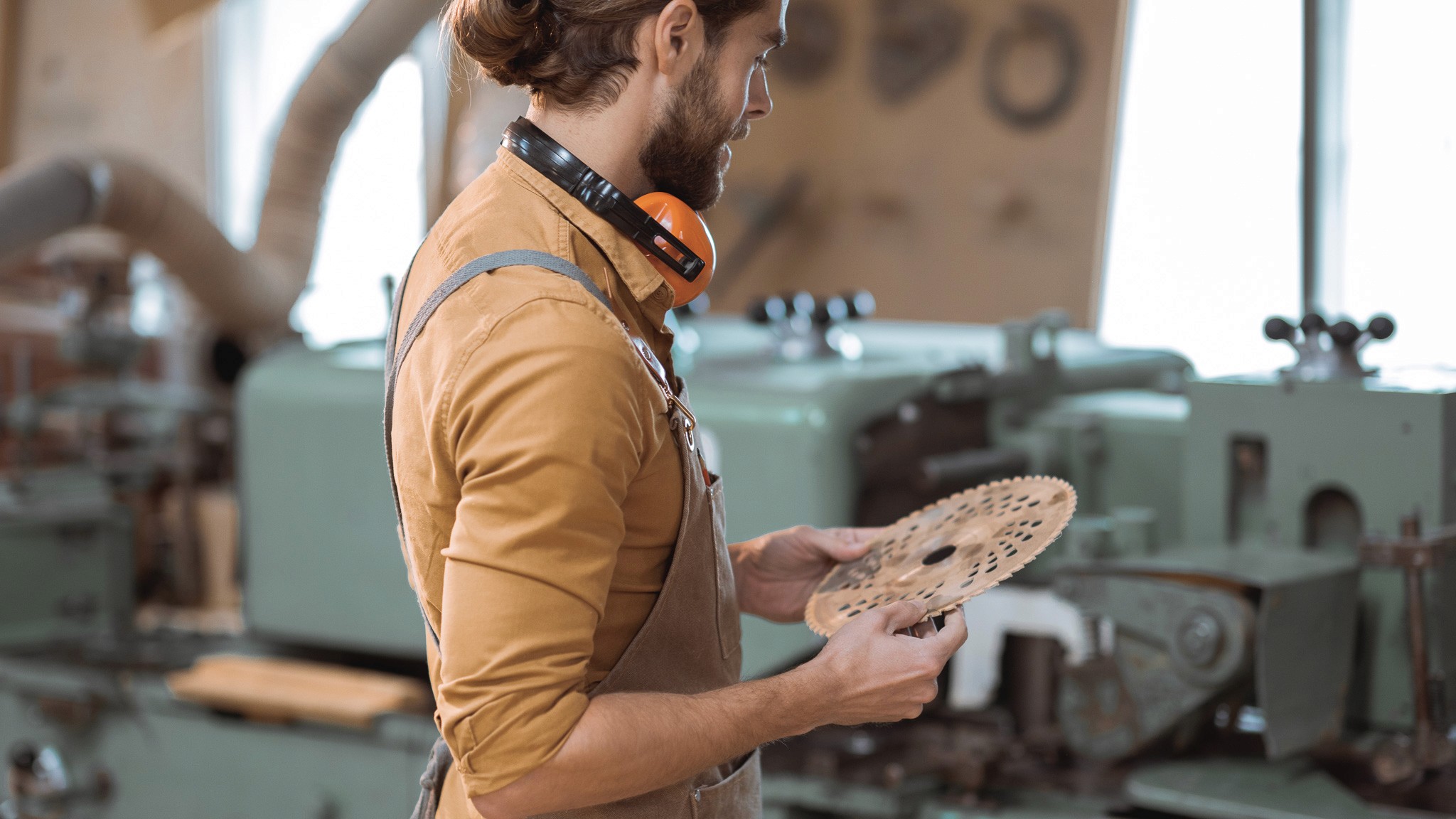 Writer holds a saw blade in hand in a workshop