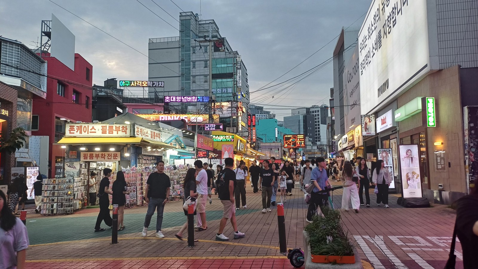 A Hongdae street in Seoul, crowded with shoppers under stacked storefront signage.