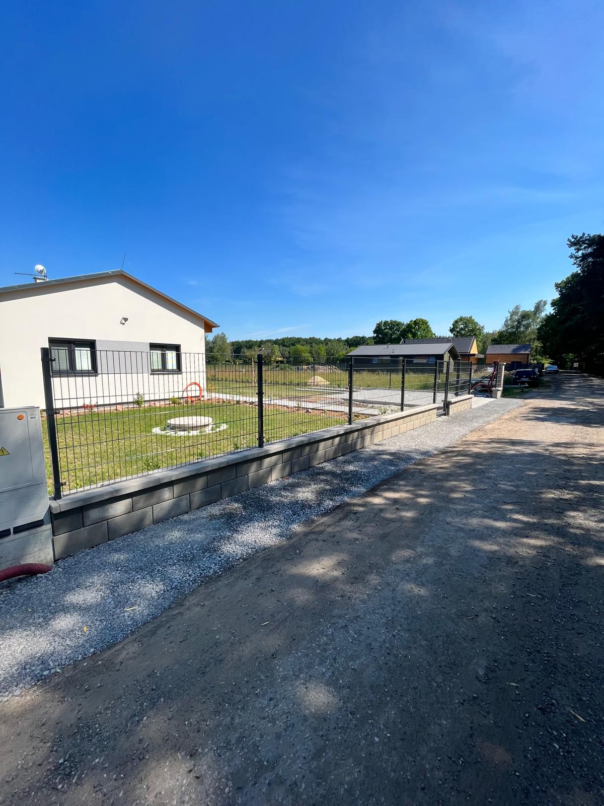 Moderní rodinný dům se zahradou a kovovým plotem. Modrá obloha.