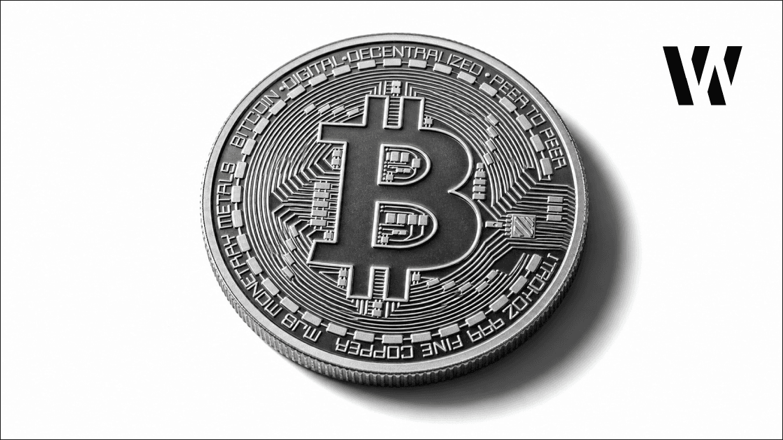 Close overhead view of a Bitcoin coin with engraved symbol on a white studio surface with sharp downward shadow.