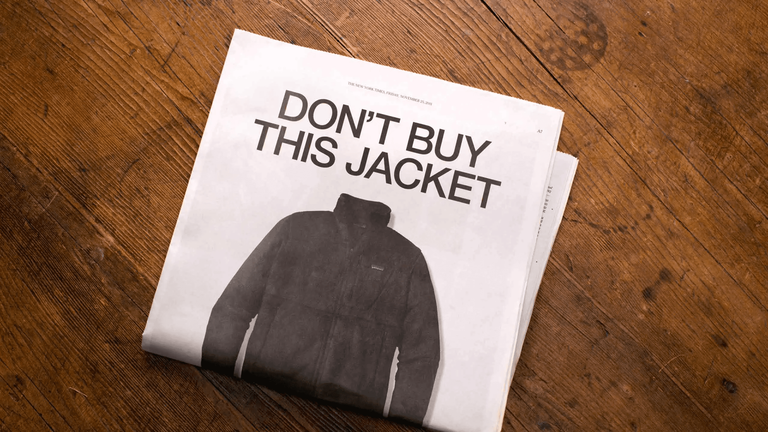 A newspaper on a wooden table showing Patagonia's famous "Don't Buy this Jacket" ad