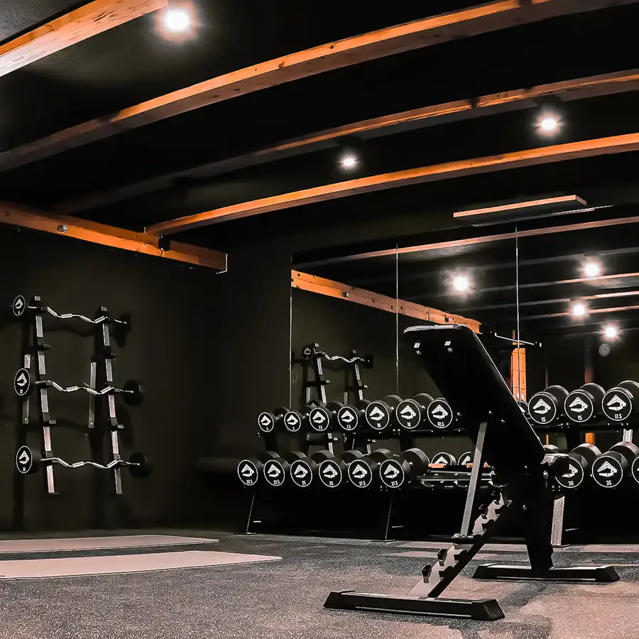 Fitnessraum mit Hantelständern, Schrägbank und Spiegelwand unter Holzbalken