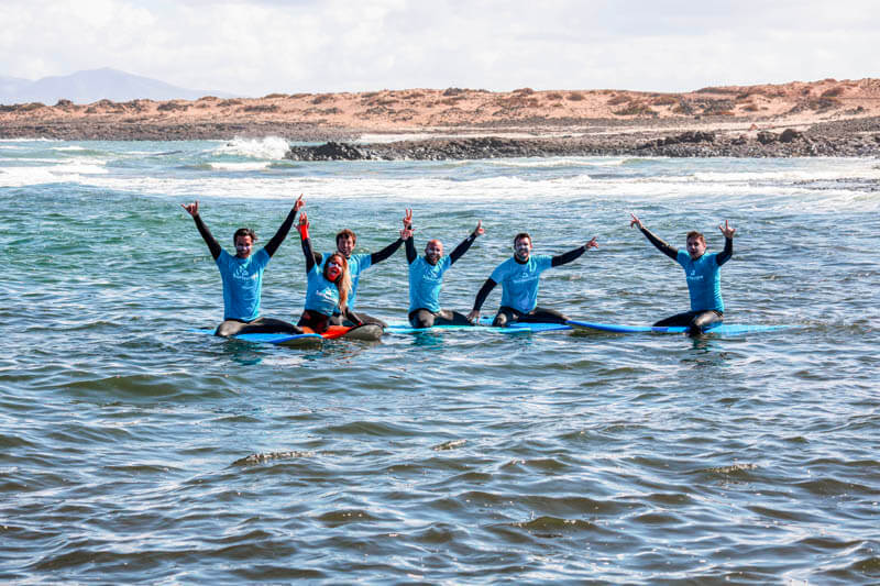 Grupo de surfistas sobre sus tablas, con los brazos en alto