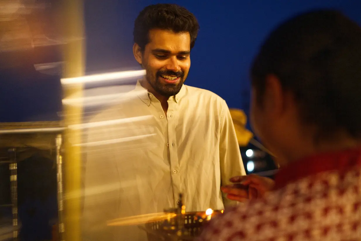 Groom smiling during an evening wedding celebration at Vedic Village Alleppey, with a traditional oil lamp lit nearby