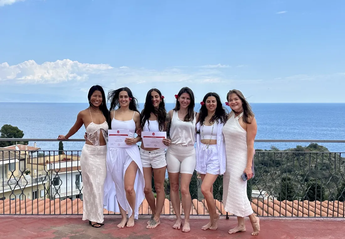 Group of happy graduates holding their yoga teacher training certificates overlooking the ocean after completion.