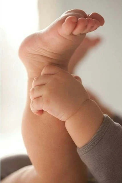 Baby hand wrapped around an adult finger in soft window light