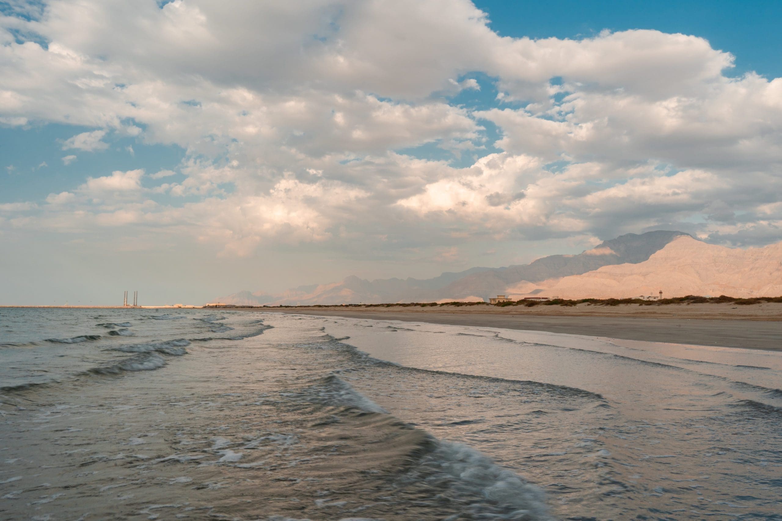 Calm waves along the peaceful shoreline, with a blue sky and white clouds.