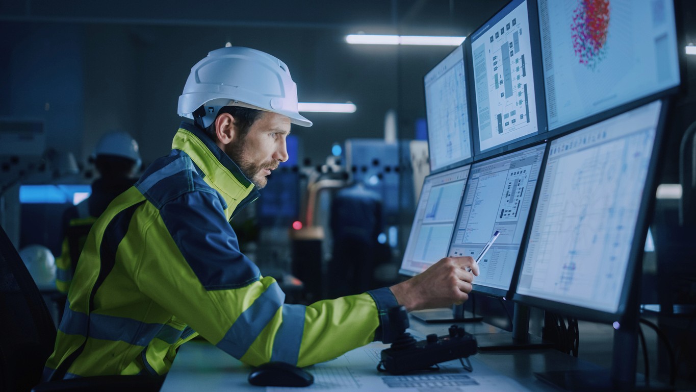 A man with a hard hat examines multiple monitor displays