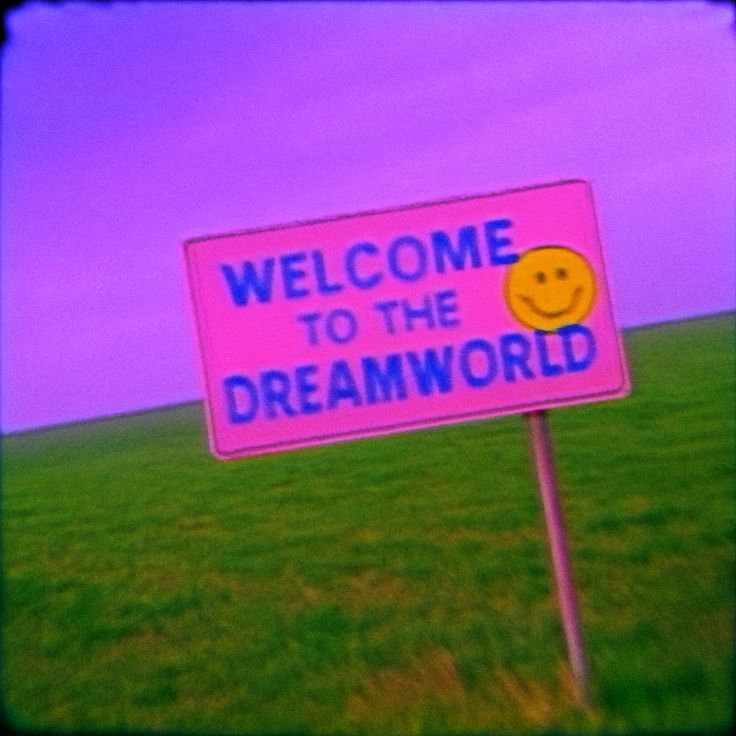 Pink sign reading Welcome to the Dreamworld with a smiley face in a grassy field